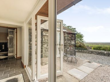 A hallway with tiled floor opens to a stone courtyard with outdoor table and chairs at Y Becws in Llanbedr near Harlech