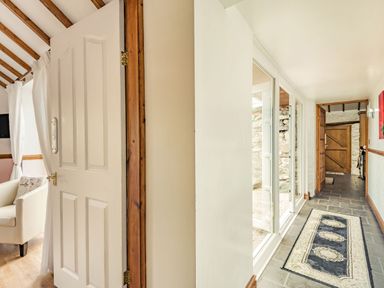 A hallway with stone floor tiles and a rug with three medallions and a seating area with a white armchair at Y Becws in Llanbedr near Harlech