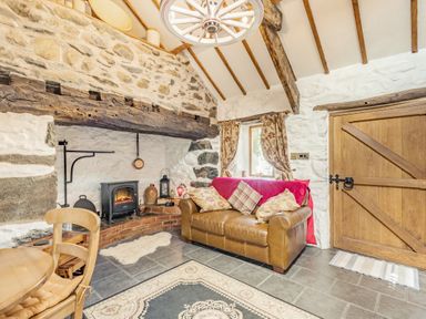 A living room with a leather sofa and cushions near a wood stove fireplace and wooden door at Y Becws in Llanbedr near Harlech