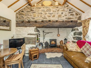 A living room with a stone fireplace wooden beam a brown leather sofa and a small wooden dining table at Y Becws in Llanbedr near Harlech
