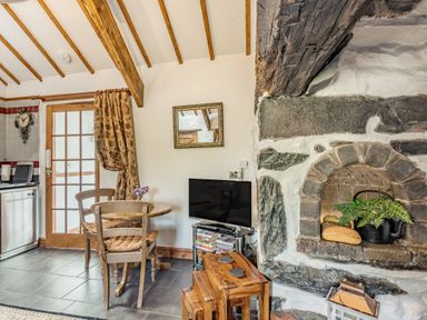 A kitchen dining area with wooden table and chairs a television stone fireplace with plant and bread at Y Becws Llanbedr near Harlech