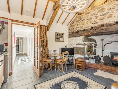 A dining area with wooden table and chairs near a stone wall and fireplace at Y Becws in Llanbedr near Harlech