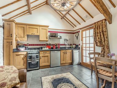 A kitchen with wooden cabinets a stove dishwasher and dining table with chairs at Y Becws in Llanbedr near Harlech