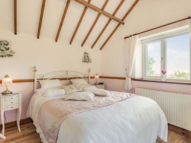 A bedroom with a double bed bedside tables lamps a window and visible wooden ceiling beams at Y Becws Llanbedr near Harlech