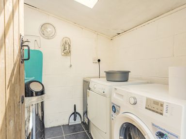 A laundry room with washing machines iron iron board and dustpan at Y Becws in Llanbedr near Harlech