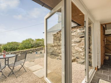 A glass door opening to a gravel patio with a metal table and chairs and a stone wall at Y Becws in Llanbedr near Harlech