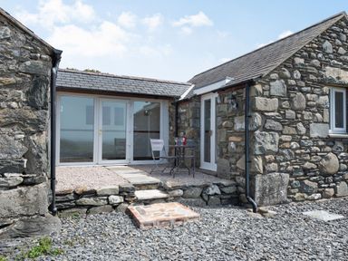 An outdoor stone patio with a small table and two chairs in front of a stone cottage at Y Becws in Llanbedr near Harlech