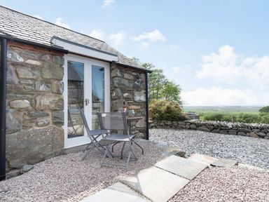An outdoor seating area with a table and two chairs outside a stone building at Y Becws in Llanbedr near Harlech