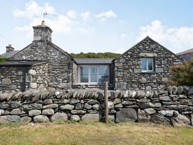A stone house with a stone wall in front and a small patio with chairs at Y Becws in Llanbedr near Harlech