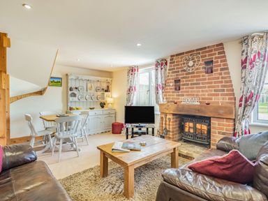 A living room with a wood burning stove fireplace a wooden coffee table leather sofas a dining table with chairs and a white cabinet at Harvest Moon in Grundisburgh