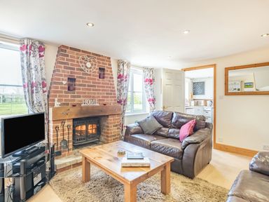 A living room with a brick fireplace a wooden coffee table two leather sofas and a television at Harvest Moon in Grundisburgh