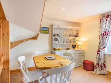 A dining area with a wooden table and white chairs next to a white dresser with plates and a lamp at Harvest Moon in Grundisburgh