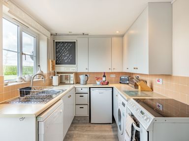 A kitchen with white cabinets, a fridge, stove, washing machine, microwave, kettle, and a window at Harvest Moon in Grundisburgh