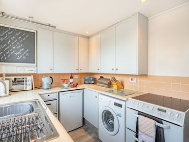 A kitchen with a sink and dish rack a microwave kettle toaster washing machine stove and cabinets at Harvest Moon in Grundisburgh