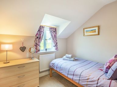 A small bedroom with a single bed a chest of drawers a window with purple curtains and a framed picture on the wall at Harvest Moon in Grundisburgh