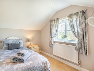 A bedroom with a bed, nightstand with lamp, window with curtains and a radiator at Harvest Moon in Grundisburgh