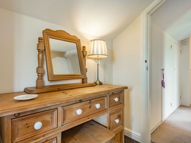 A wooden dressing table with a mirror and a lamp next to a hallway with white closets at Harvest Moon in Grundisburgh