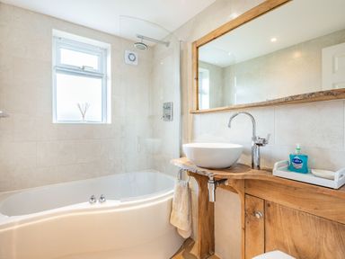 A bathroom with a bathtub shower combination a wooden vanity with a vessel sink and a large mirror at Harvest Moon in Grundisburgh