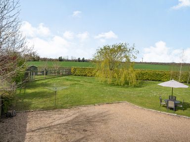 A garden with a gravel area, a round table with chairs and umbrella, a clothesline, a small shed, trees and hedges at Harvest Moon in Grundisburgh