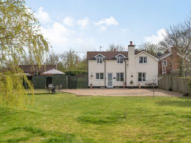 A view of a two-story house with a tiled roof and a large garden with a table and chairs at Harvest Moon in Grundisburgh