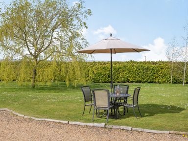 An outdoor garden with a round table under an umbrella and four chairs on grass at Harvest Moon in Grundisburgh