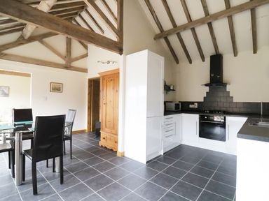 A kitchen and dining area with a glass table black chairs white cabinets and wooden beams at Jackos Barn in Homersfield