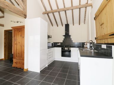 A kitchen with white cabinets black countertops wooden beams on ceiling and black tile floor at Jacko's Barn in Homersfield