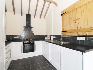 A kitchen with white cabinets black countertops black tiled backsplash wooden wall cupboards and exposed ceiling beams at Jacko's Barn in Homersfield
