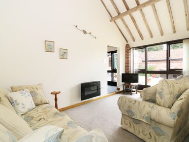 A living room with patterned sofas small wooden side tables wall mounted heater and large windows at Jacko's Barn in Homersfield