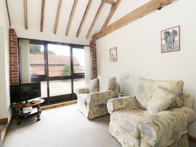 A sitting room with two armchairs a small tv on a wooden table and exposed wooden beams at Jackos Barn in Homersfield