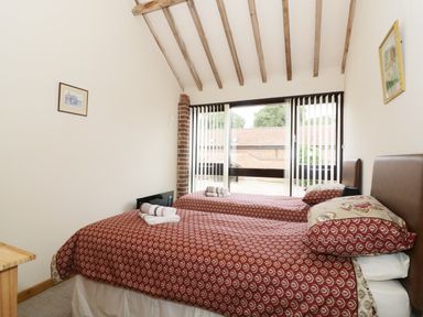 A bedroom with two single beds covered in patterned red bedding and towels on top at Jacko's Barn in Homersfield