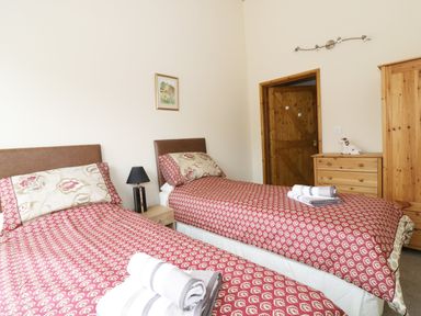 A bedroom with two single beds side by side red patterned bedding and folded towels on each bed a wooden door and wooden furniture with a small lamp and a framed picture on the wall at Jacko's Barn in Homersfield