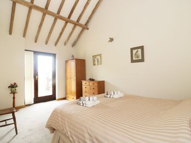 A bedroom with a double bed folded towels on the bed wooden wardrobe and chest of drawers near glass door at Jacko's Barn in Homersfield