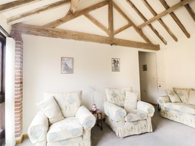 A sitting room with two armchairs a sofa wooden beams on the ceiling and framed horse pictures on the wall at Jacko's Barn in Homersfield