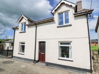 The exterior of a two story house with white walls a brown front door and multiple windows at Green Cottage in Pant-y-Dwr near Rhayader