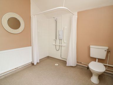 A bathroom with a shower area with curtain a toilet a round wall mirror and a radiator at Green Cottage Pant-y-Dwr near Rhayader