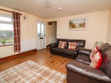 A living room with two brown leather sofas with plaid cushions a door a window with plaid curtains a framed picture and a rug on wooden floor at Green Cottage Pant-y-Dwr near Rhayader