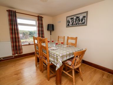 A dining room with six wooden chairs around a table covered with a plaid tablecloth and a window with plaid curtains at Green Cottage in Pant-y-Dwr near Rhayader
