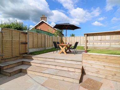A fenced backyard with a wooden table and chairs under a black umbrella at Green Cottage in Pant-y-Dwr near Rhayader