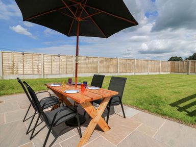An outdoor patio with a wooden table black chairs an umbrella plates and glasses in a fenced yard at Green Cottage in Pant-y-Dwr near Rhayader