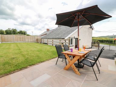 An outdoor patio area with a wooden table four chairs and a large umbrella next to a grassy lawn at Green Cottage in Pant-y-Dwr near Rhayader