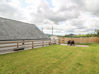 A backyard with a lawn a patio table with an umbrella and chairs and a house with a tiled roof at Green Cottage in Pant-y-Dwr near Rhayader