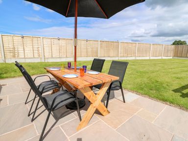 An outdoor patio with a wooden table set with plates and glasses under a large black umbrella at Green Cottage in Pant-y-Dwr near Rhayader