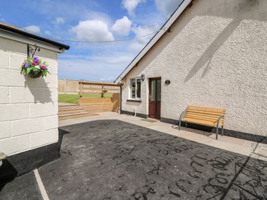 A patio area outside a building with hanging flower baskets wooden bench and steps leading to a grassy area at Green Cottage in Pant-y-Dwr near Rhayader