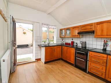 A kitchen with wooden cabinets a black countertop a stove and an open door leading outside at Green Cottage in Pant-y-Dwr near Rhayader