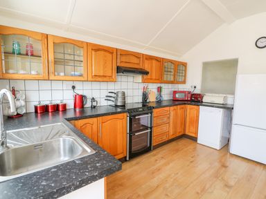 A kitchen with wooden cabinets black countertops a stove dishwasher refrigerator and red appliances at Green Cottage in Pant-y-Dwr near Rhayader