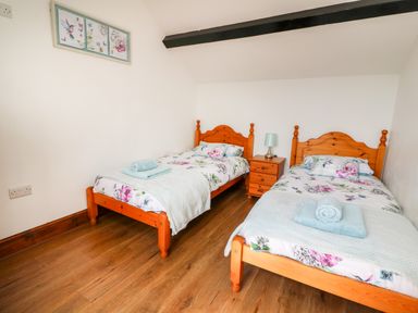 A bedroom with two wooden beds with floral bedding and a nightstand with a lamp at Green Cottage in Pant-y-Dwr near Rhayader