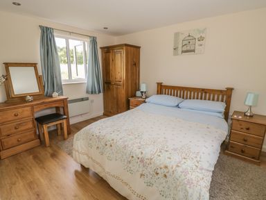 A bedroom with a double bed a wooden wardrobe and two bedside tables with lamps at Lawn Lodge in Ashleworth