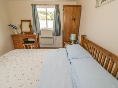 A bedroom with a wooden bed a dressing table with a mirror a small stool and a wardrobe at Lawn Lodge in Ashleworth
