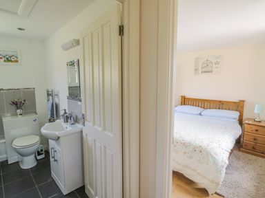 A bathroom with toilet and sink next to a bedroom with a wooden bed and wooden side table at Lawn Lodge in Ashleworth